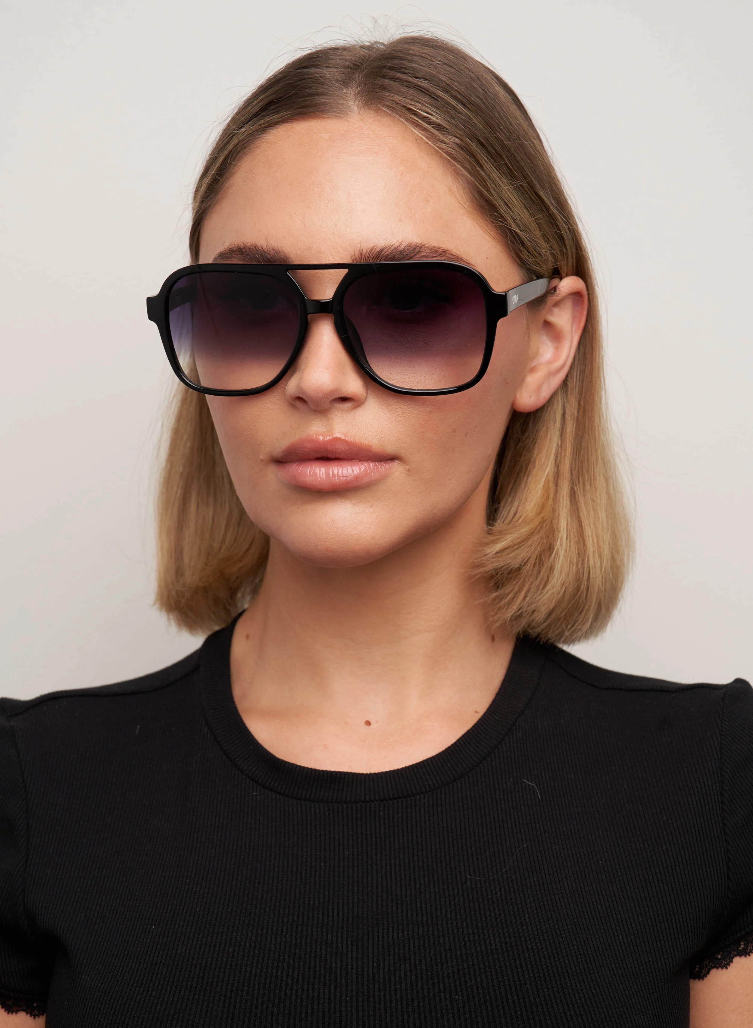 OTRA Eyewear Kori sleek minimalist aviator sunglasses in a sharp black frame featuring modern gradient smoke fade lenses.